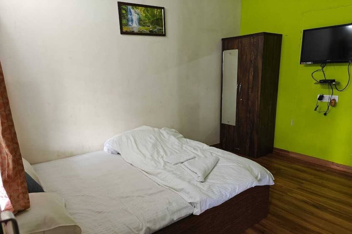 Una cama individual con ropa de cama blanca en una habitación con paredes verdes y suelo de madera.