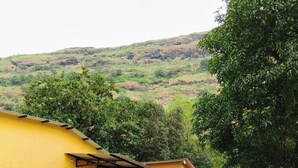 A yellow building with a staircase leading to a door, surrounded by greenery and hills in the background. - Rutuvan Resort Girivan (Paud)