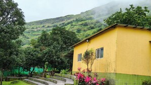 A yellow building with a green base, surrounded by lush greenery and a winding staircase leading to a higher level. - Rutuvan Resort Girivan (Paud)