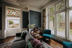 A living room with a sofa, armchairs, a coffee table, and a view of the outdoors through large windows. - The Pheasant Lodge (Grange-over-Sands)