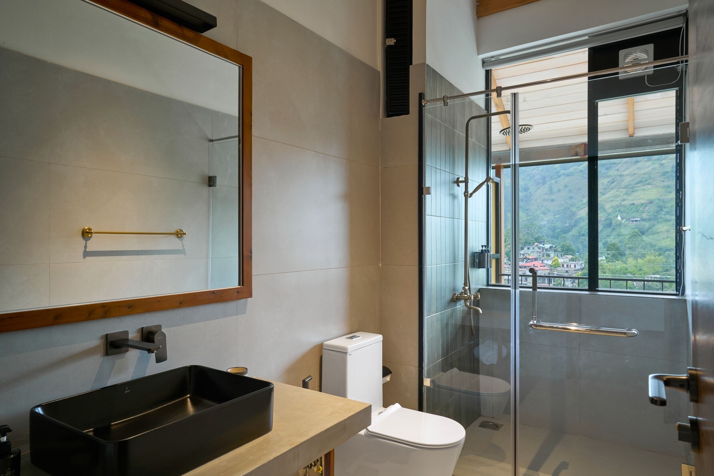 Un baño moderno con un espejo grande, un lavabo negro, un inodoro y una ducha con mampara de vidrio.