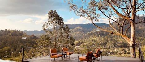 A poolside area with lounge chairs and a table, overlooking a mountainous landscape.