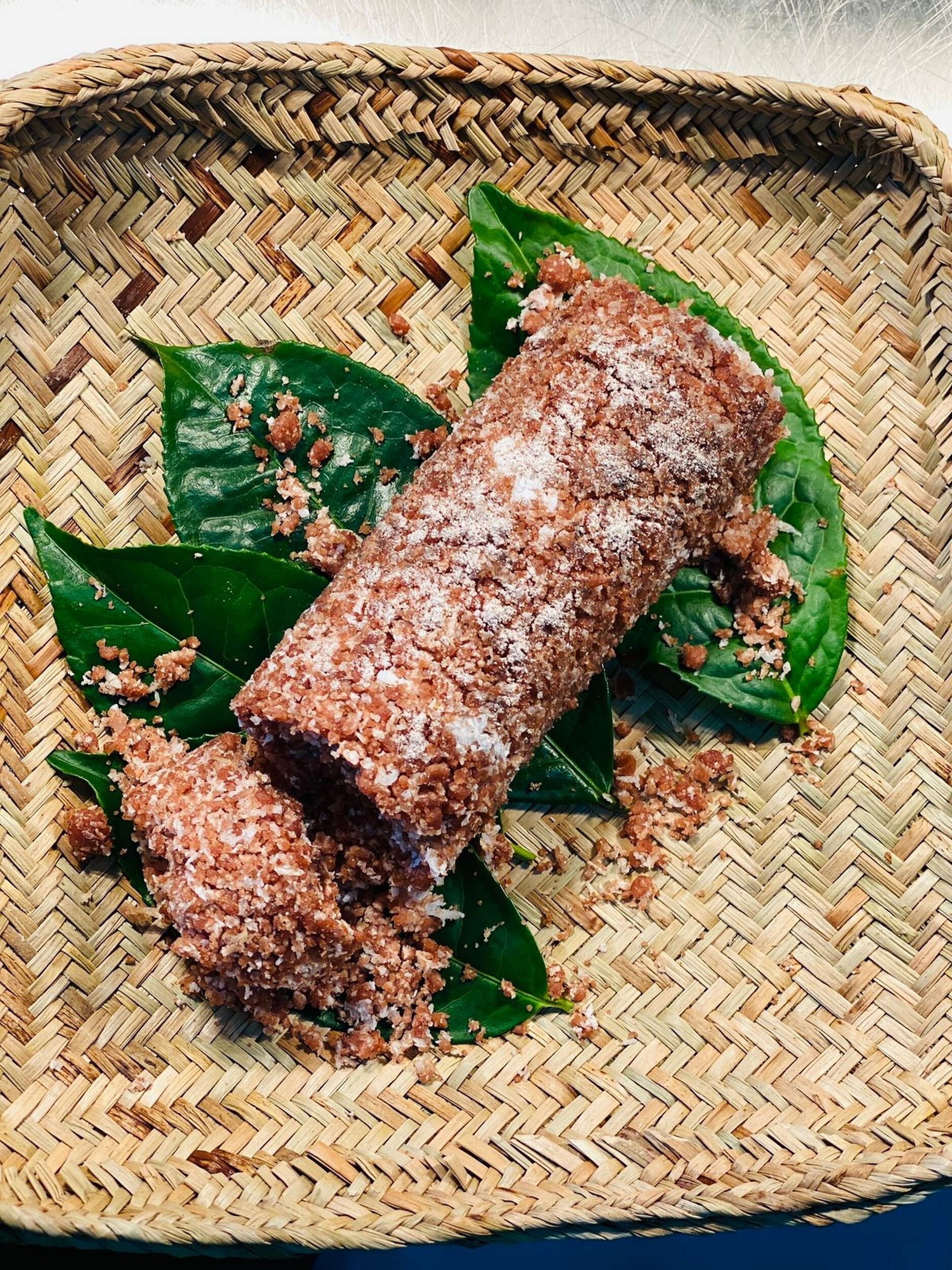 A woven basket containing a rolled food item, possibly a dessert, with a green leaf underneath.