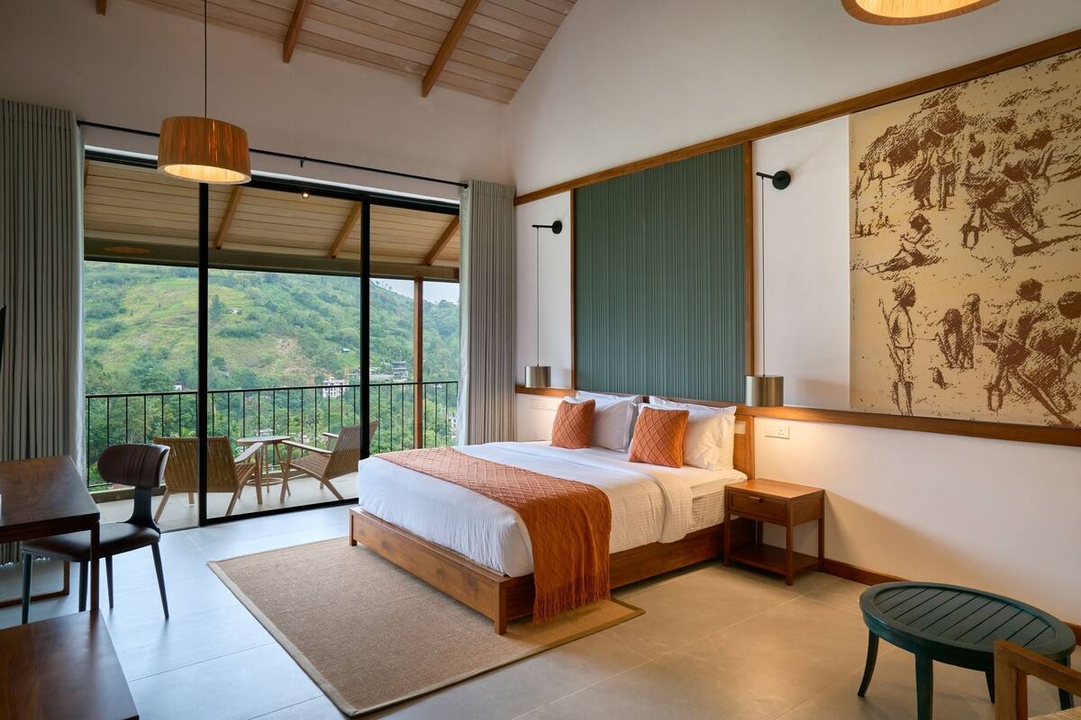 Une chambre spacieuse avec un grand lit, un balcon avec des chaises et une vue sur l’extérieur.