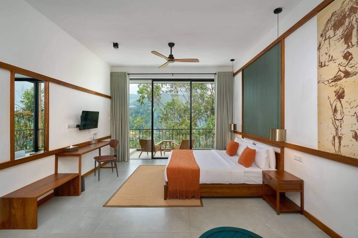 Une chambre d’hôtel moderne dotée d’un grand lit, d’un bureau, d’une chaise et d’un balcon offrant une vue sur les arbres.