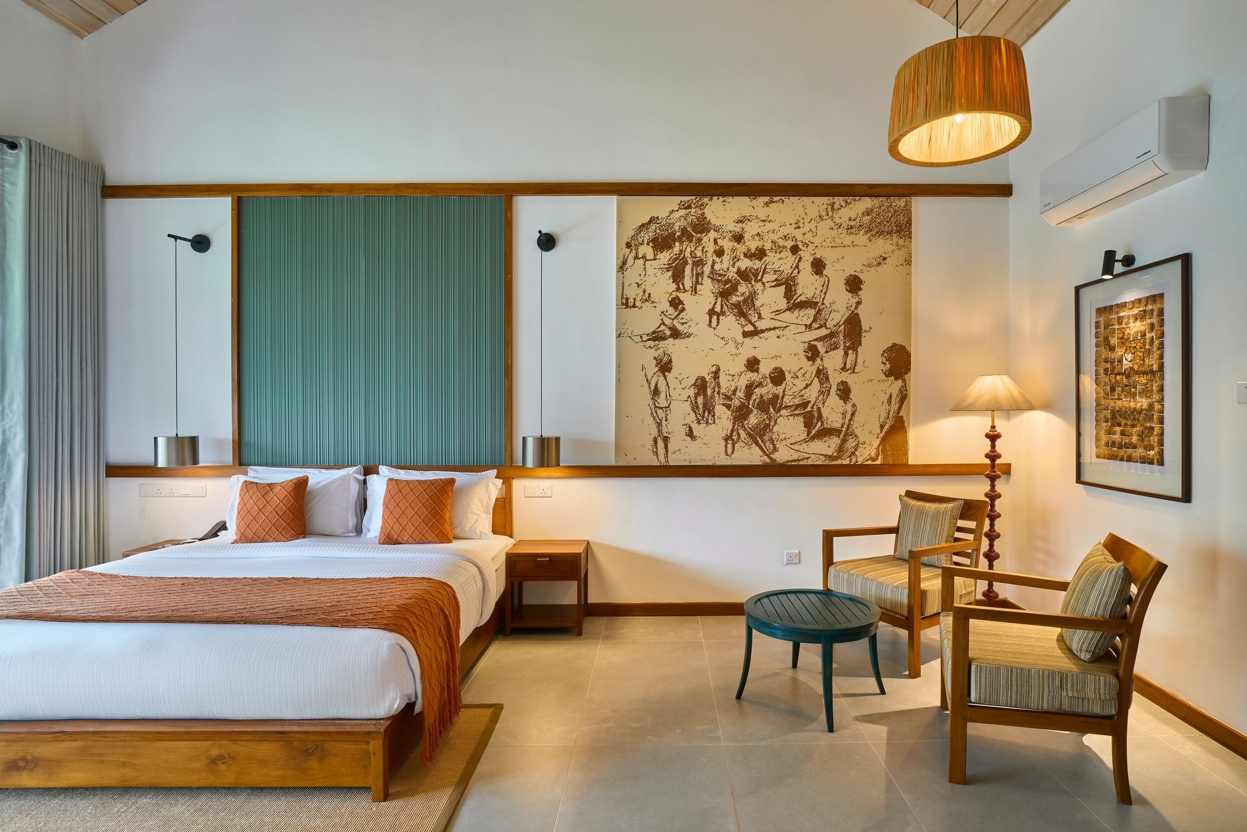 Habitación de hotel con una cama de madera, un muro verde decorativo, una obra de arte grande, un escritorio con sillas y una lámpara colgante.