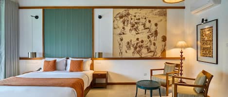Habitación de hotel con una cama de madera, un muro verde decorativo, una obra de arte grande, un escritorio con sillas y una lámpara colgante.