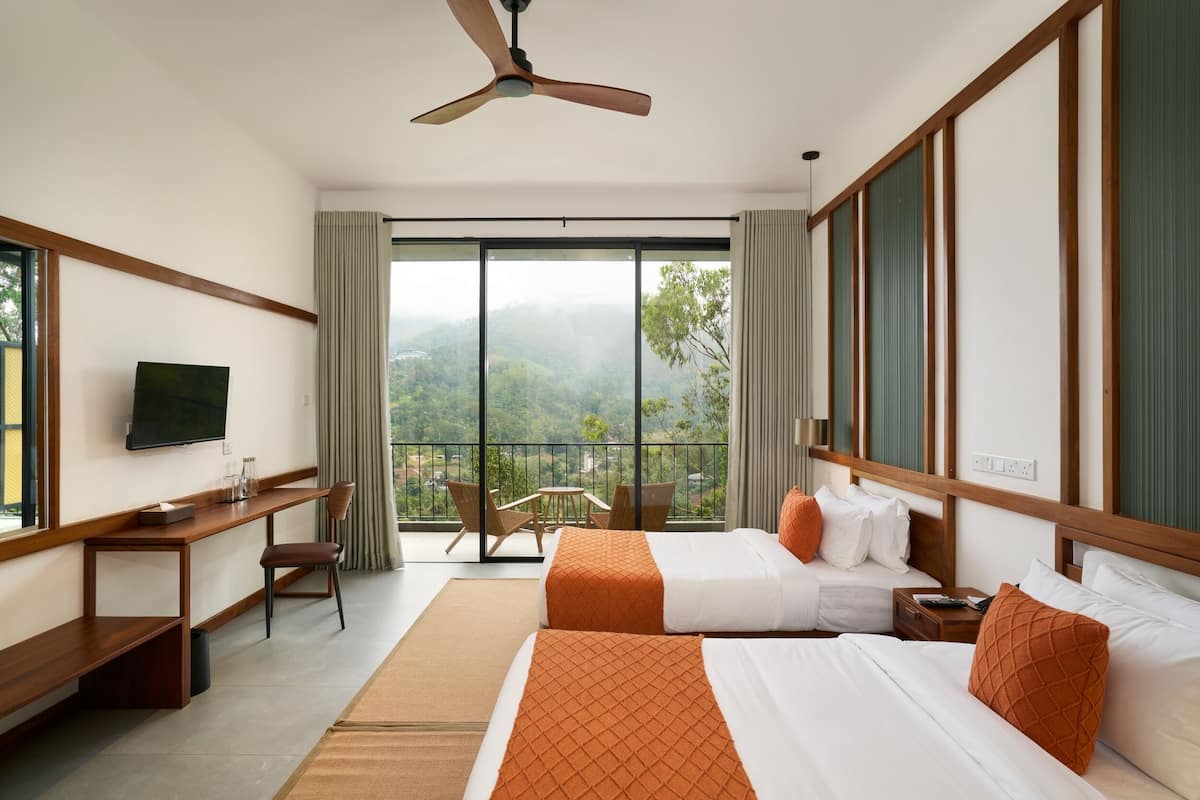 Une chambre d’hôtel avec deux lits, un bureau, une télévision et un balcon offrant une vue sur les montagnes.