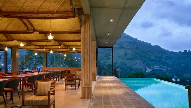 Un área de comedor al aire libre con mesas y sillas, una piscina y vistas a un paisaje montañoso.