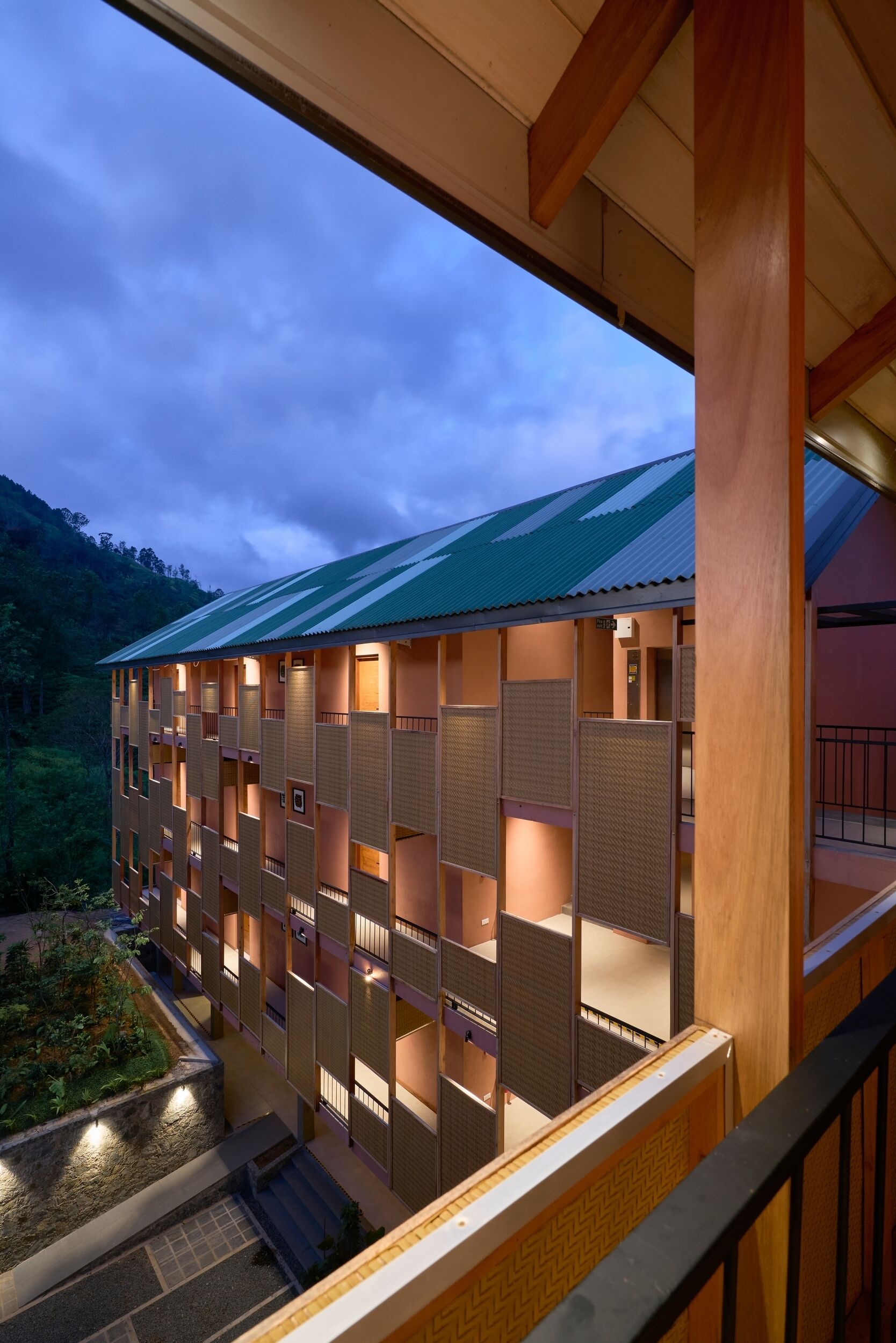 Un hotel de varios pisos con techo verde, paneles de madera y vistas a un paisaje montañoso.