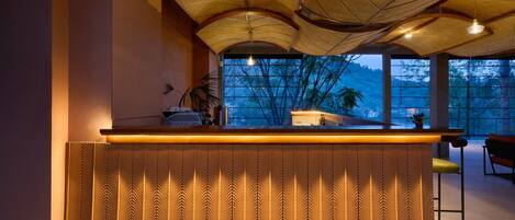 A reception desk with a patterned design, a ceiling with woven patterns, and a view of trees through large windows.