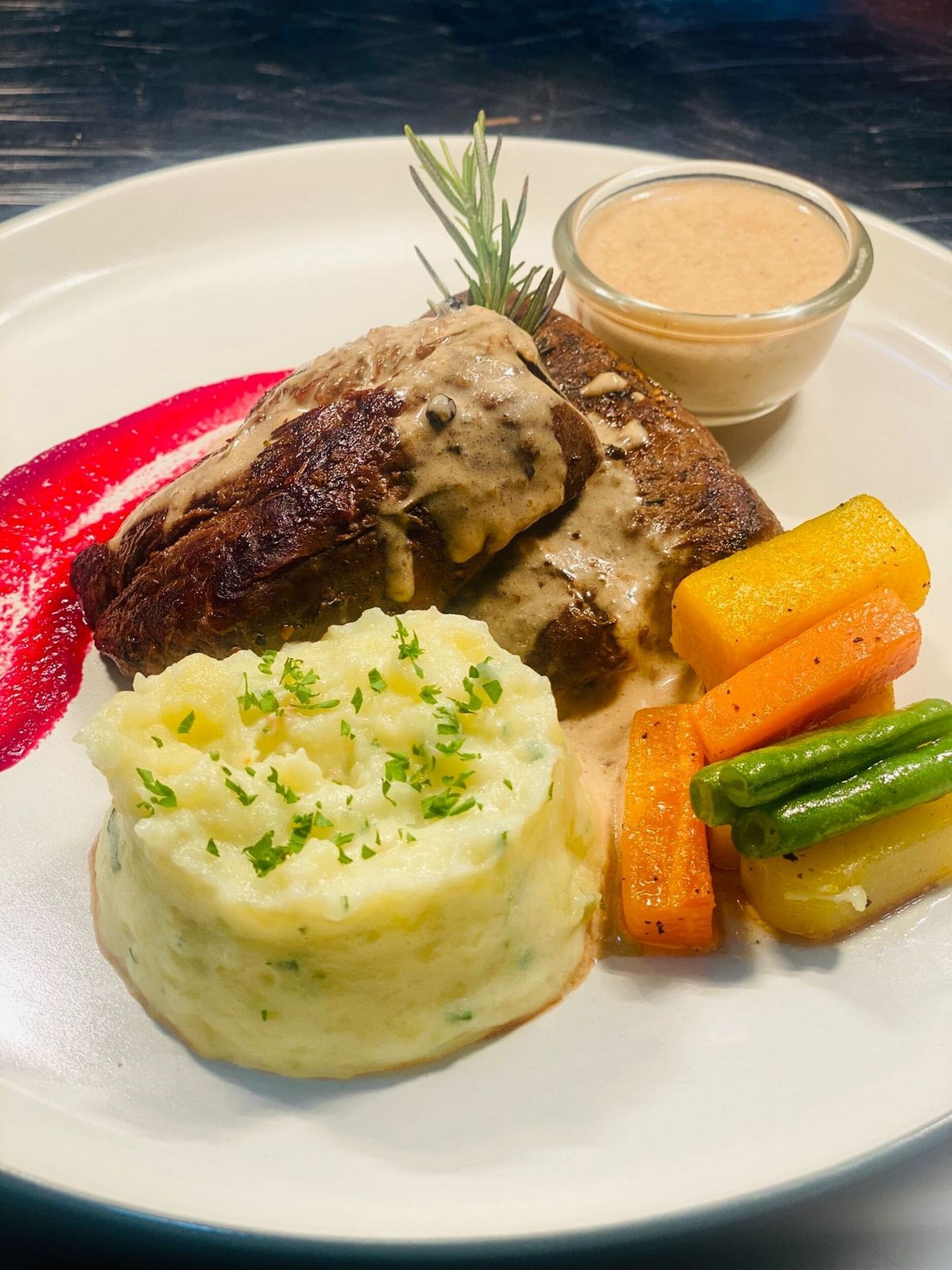 A plate with a steak, mashed potatoes, carrots, green beans, and a sauce.