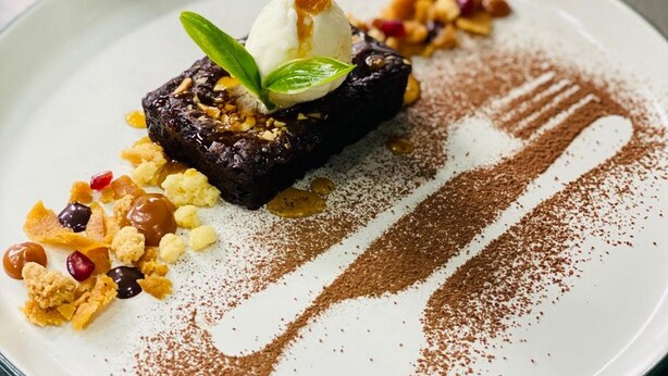 Une assiette à dessert avec un gâteau au chocolat, une boule de glace et diverses garnitures, le tout présenté sur une assiette blanche.