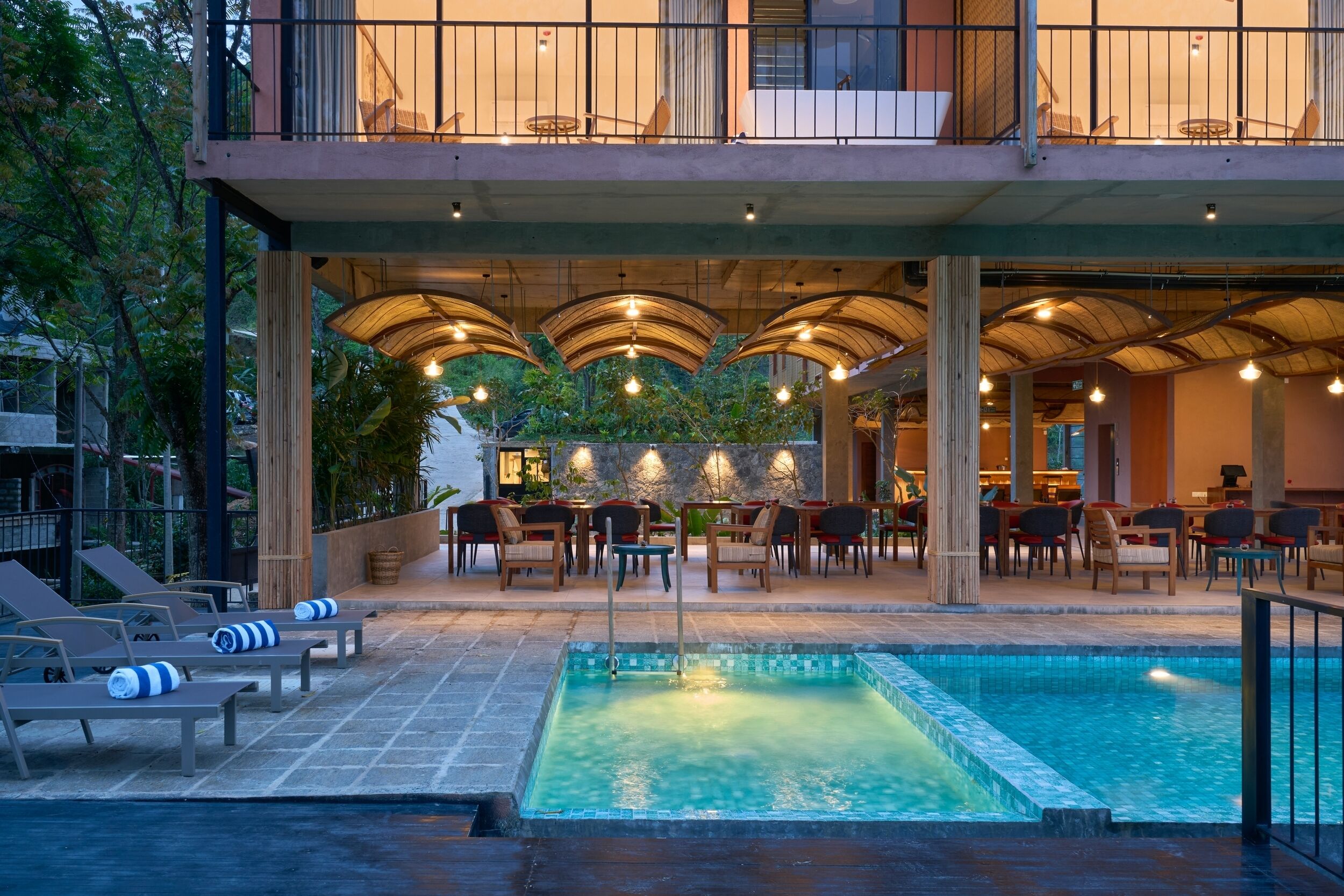 Un área de piscina en la azotea con sillones, una piscina y un comedor al aire libre con mesas y sillas.