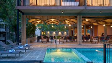 A rooftop pool area with lounge chairs, a pool, and an outdoor dining area with tables and chairs.