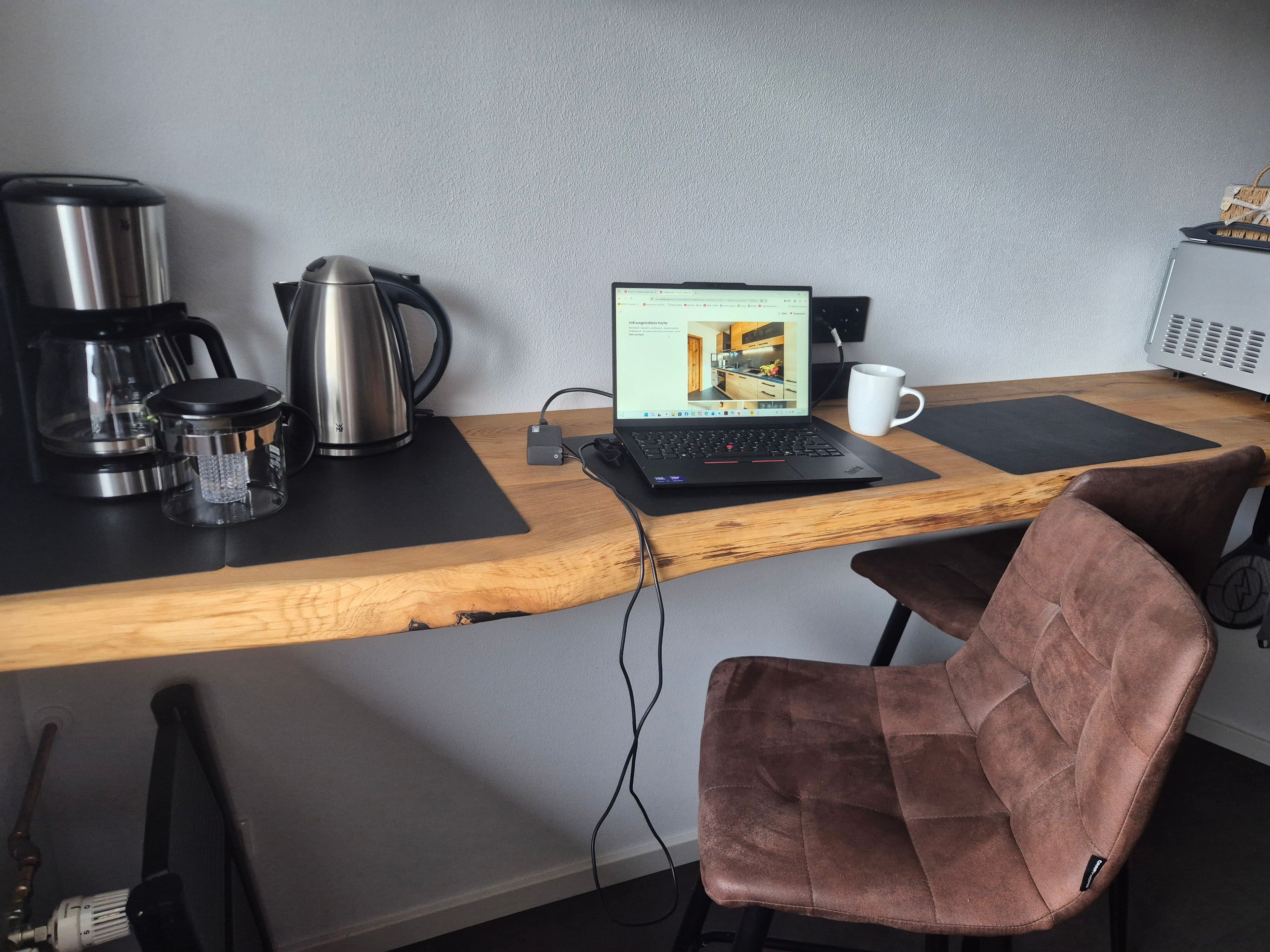 Un bureau en bois avec un ordinateur portable, une machine à café, une tasse et une chaise.