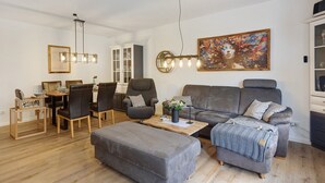 Un salon moderne avec un canapé gris, une table basse en bois, un coin repas avec une table et des chaises, et un tableau accroché au mur.