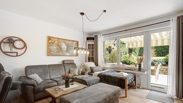 Un salon moderne avec un canapé, un pouf et une table basse. Il y a un tableau au mur et une horloge.