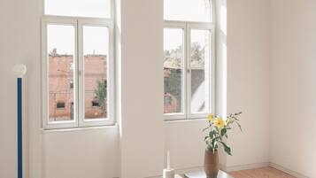 Una habitación con dos ventanas arqueadas, un sofá verde, una pequeña mesa con un jarrón de flores y una lámpara de pie azul alta.
