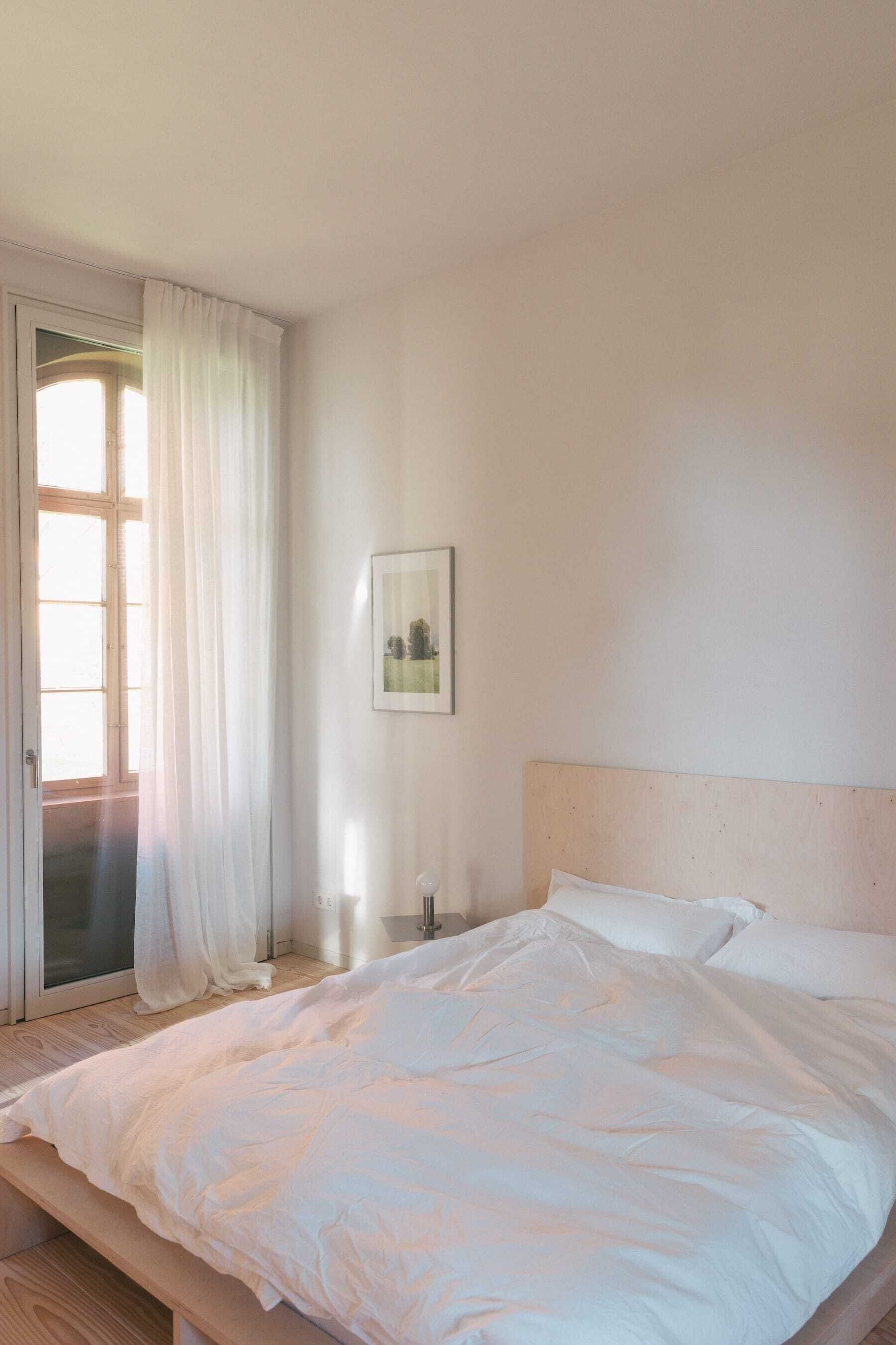 A bedroom with a large bed, a window with sheer curtains, and a framed picture on the wall.
