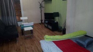 Ein Zimmer mit einem Bett, einem Sessel, einem Schreibtisch, einem Fernseher und einer Pflanze.