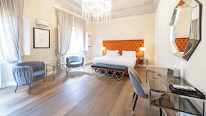 Une chambre d’hôtel avec un grand lit, un bureau, une chaise, un banc et un lustre.