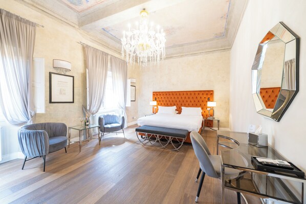 Una camera d'albergo con un letto grande, una scrivania, una sedia, una panca e un lampadario.