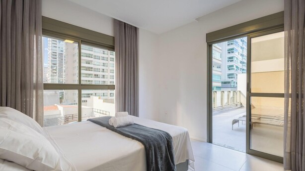 Une chambre d’hôtel avec un lit, de grandes fenêtres et un balcon offrant une vue sur la ville.