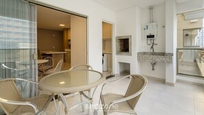 Un intérieur moderne avec une table à manger en verre, des chaises en osier, un coin cuisine et une salle de bain dotée d’une douche intégrée.