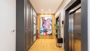 Un couloir doté d’un plancher en bois, une grande peinture abstraite au mur et deux ascenseurs.