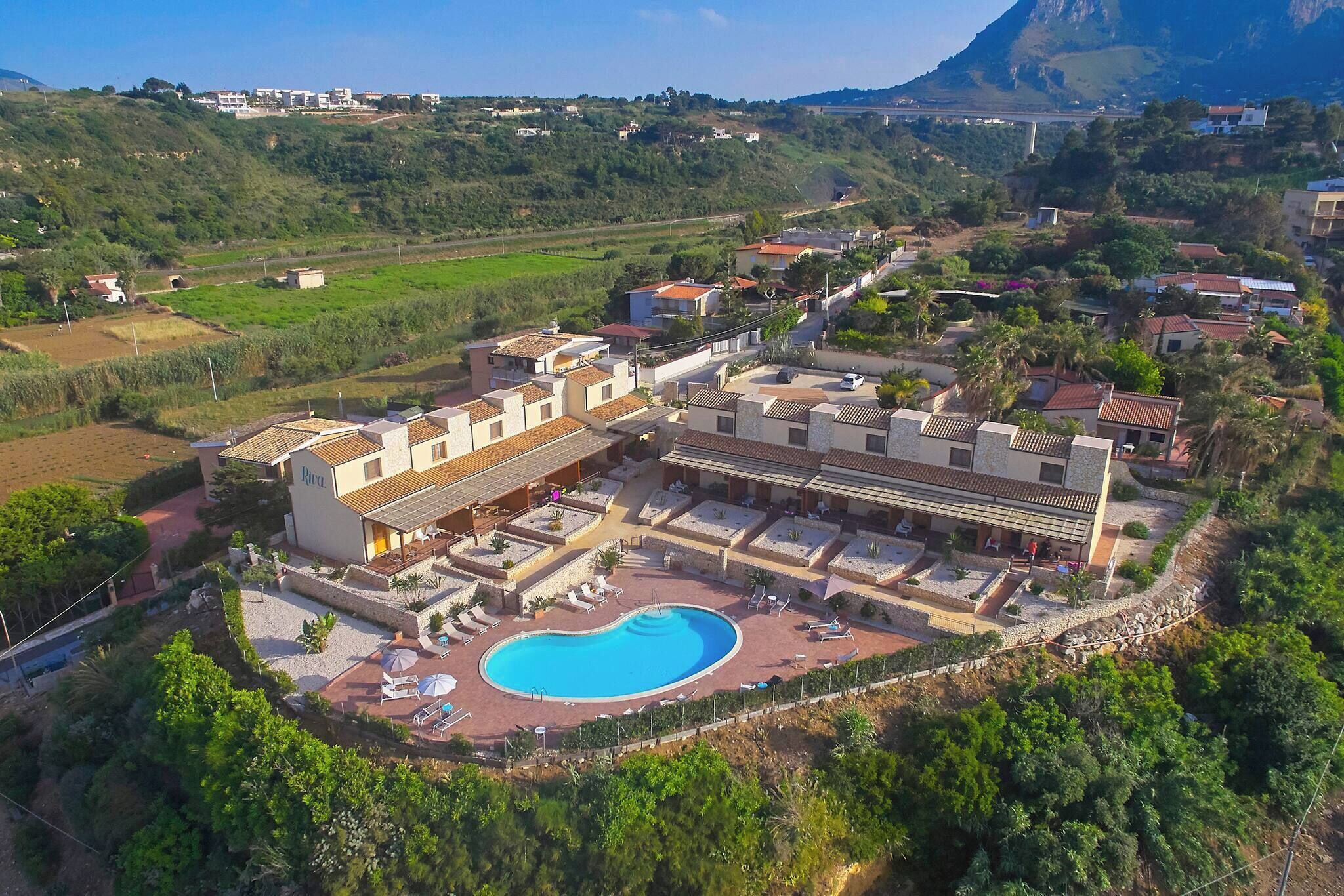 An aerial view of a resort with multiple buildings, a swimming pool, and surrounding greenery.