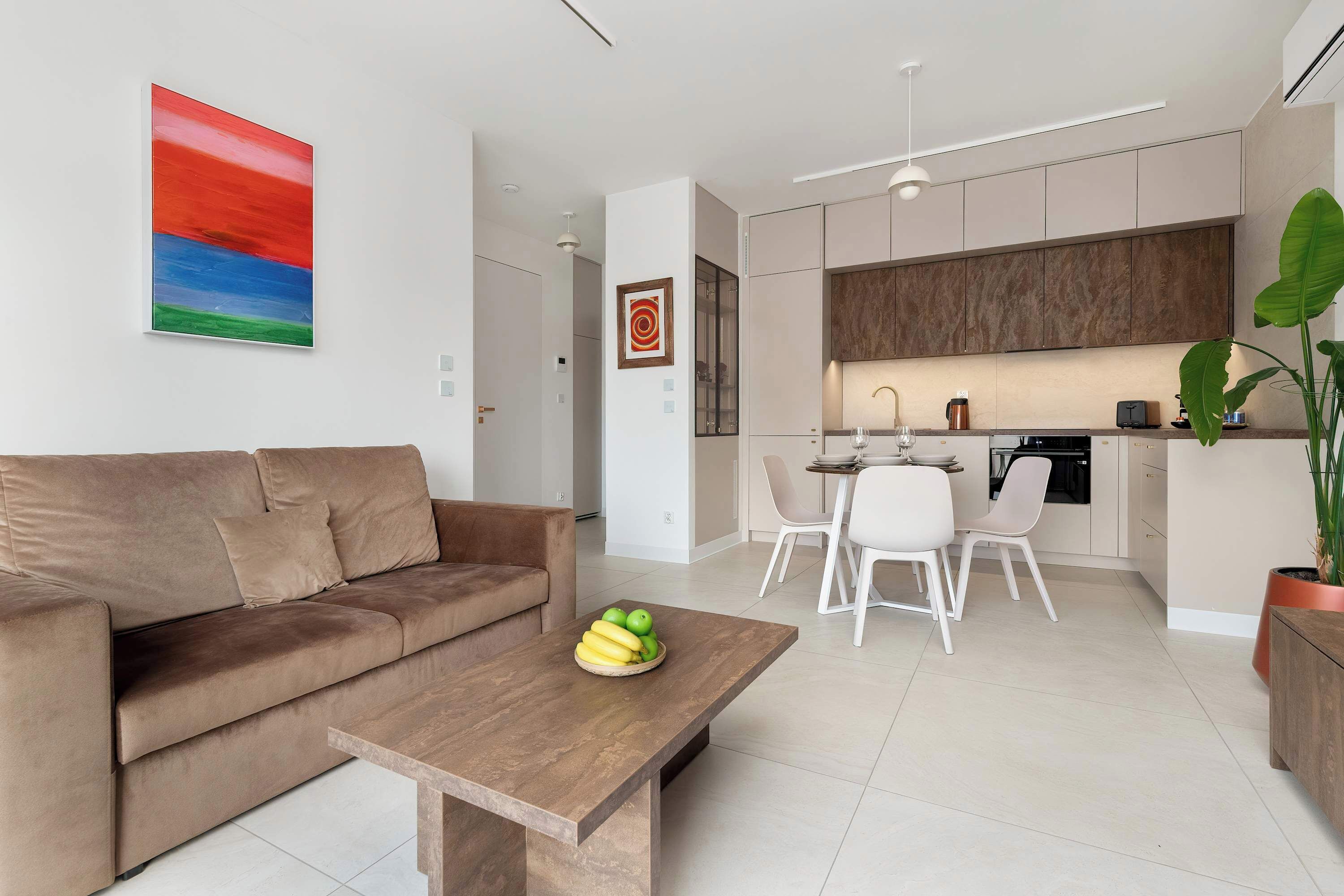 A modern living room with a wooden coffee table centered in front of a sofa. Large windows brighten the space while decorative pieces add personality. The simple layout keeps the room open and welcoming.