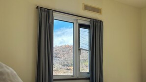 A bedroom with a bed, a window with curtains, and a view of trees outside.