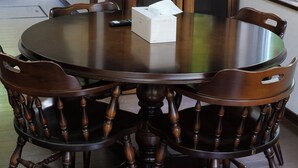 A round wooden dining table with chairs, a cabinet with glass doors, and a window with a view of greenery.