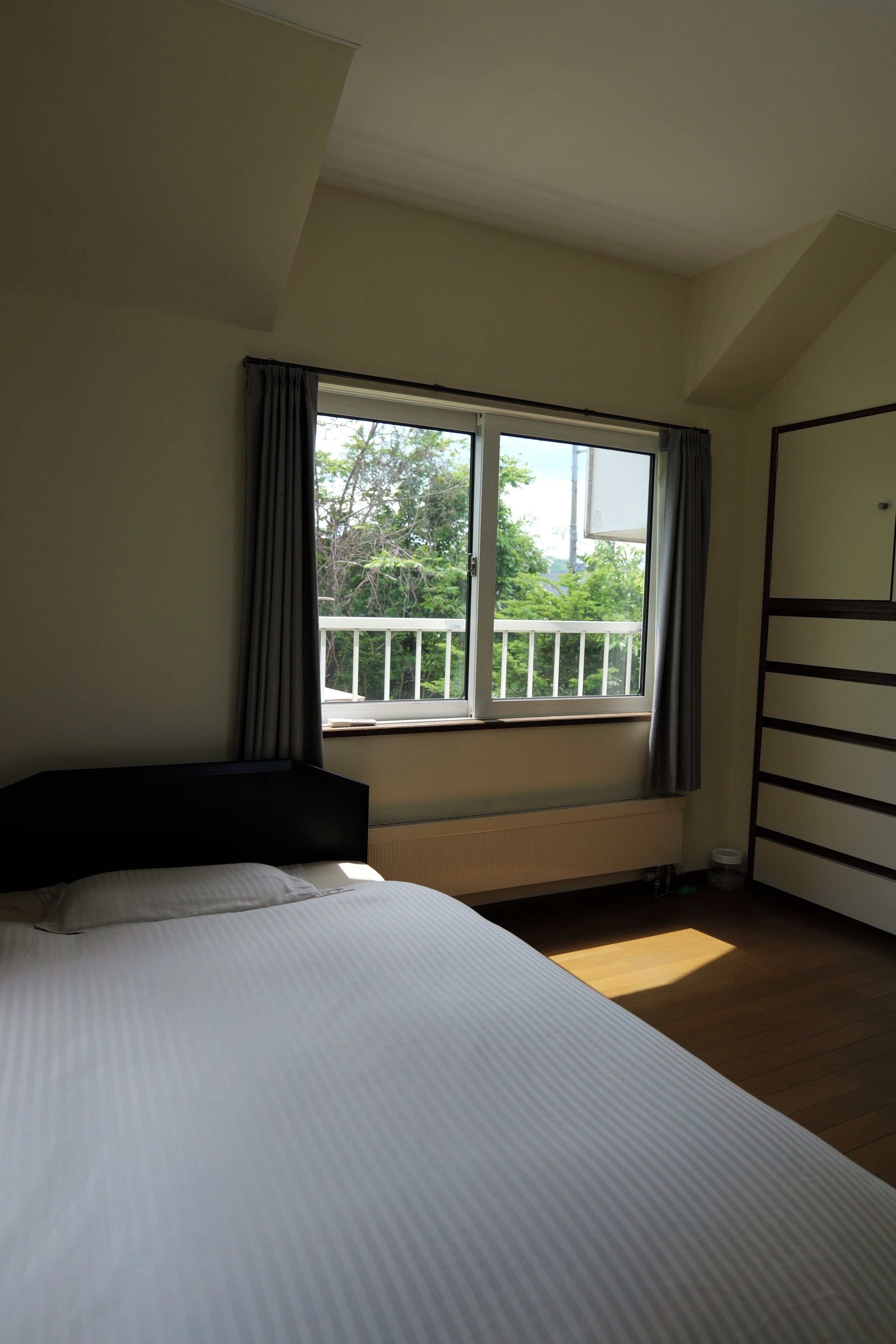 Quarto com cama, janela com vista para o verde, radiador e guarda-roupa.