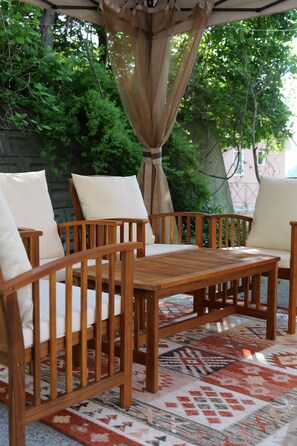 Una mesa y sillas de madera con cojines blancos, un tapete estampado y una cortina.
