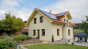 Una casa de dos pisos con techo inclinado, paneles solares y jardín de piedra.
