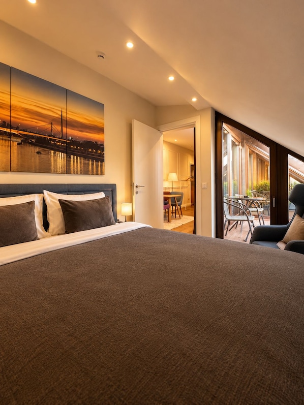 Ein Hotelzimmer mit einem großen Bett, Blick auf die Stadt und einem Balkon mit Sitzgelegenheit.