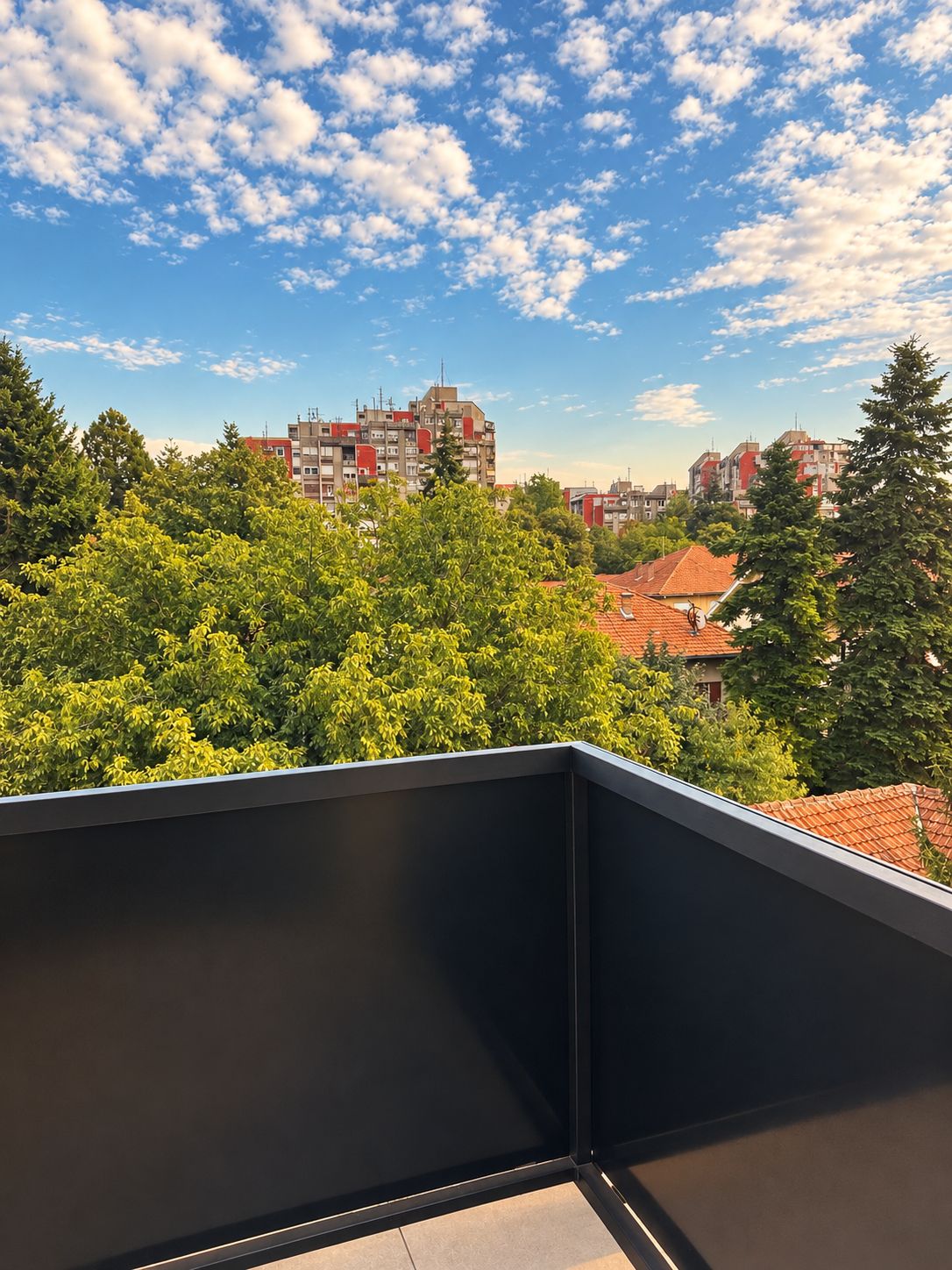 A balcony with a view of a cityscape, including buildings and trees.