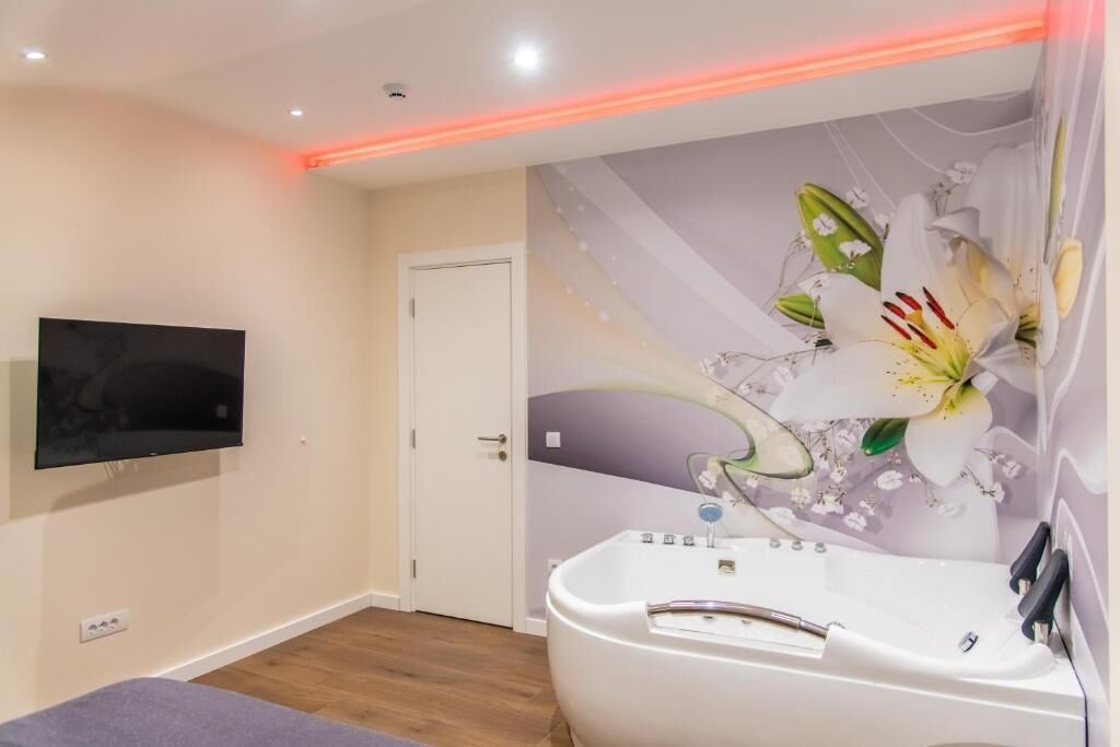 Une salle de bain moderne avec une baignoire, un téléviseur à écran plat fixé au mur et une fresque murale à motifs floraux.
