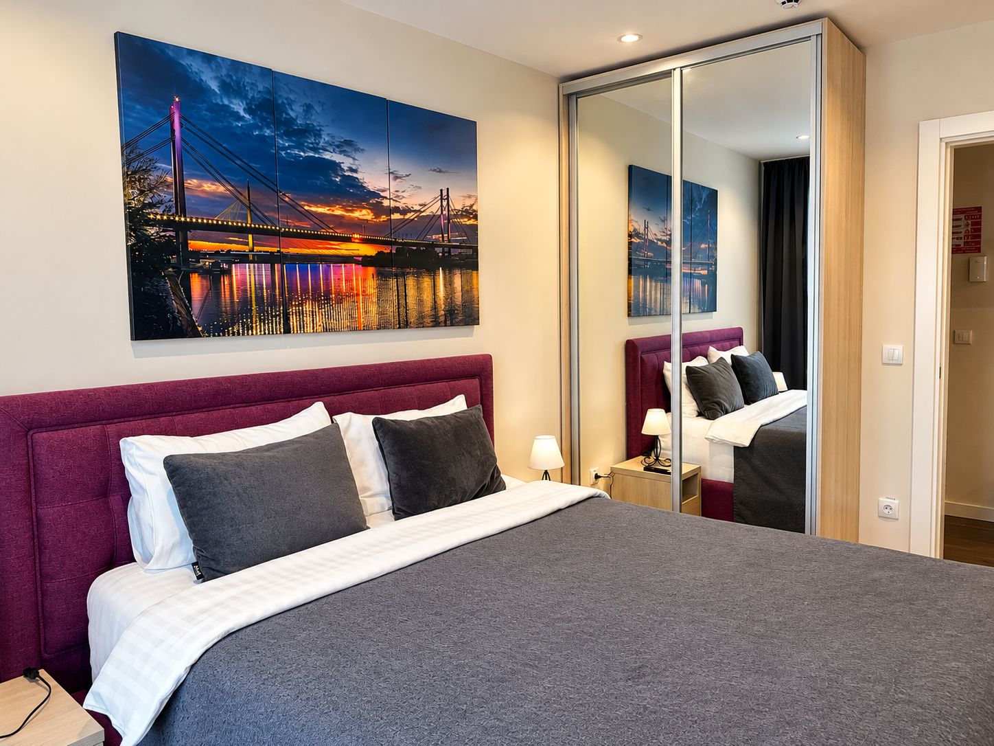 Una habitación de hotel con una cama grande, una mesita de noche, un espejo y un cuadro de un puente.