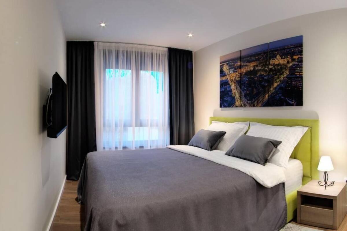 Un moderno cuarto de hotel con una cama grande, un televisor de pantalla plana montado en la pared y una pintura de paisaje urbano sobre la cama.