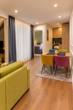 A modern living room with a dining area, wooden flooring, and a bed in the background. - Hotel Maksimum (Belgrade)