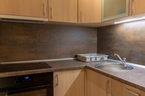 A kitchen with wooden cabinets, a built-in oven, a stainless steel sink, and a countertop with storage containers. - Hotel Maksimum (Belgrade)