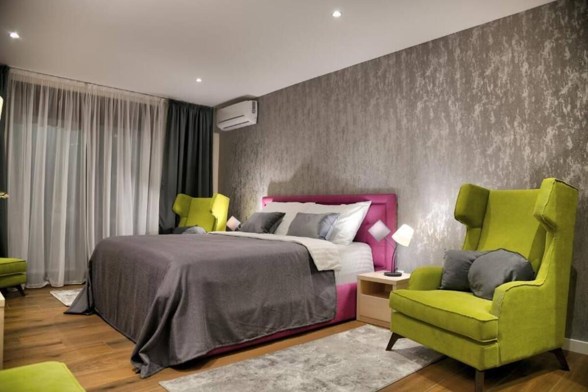 Un dormitorio moderno con una cama grande, un sillón verde, una mesita de noche y una pared gris con textura.