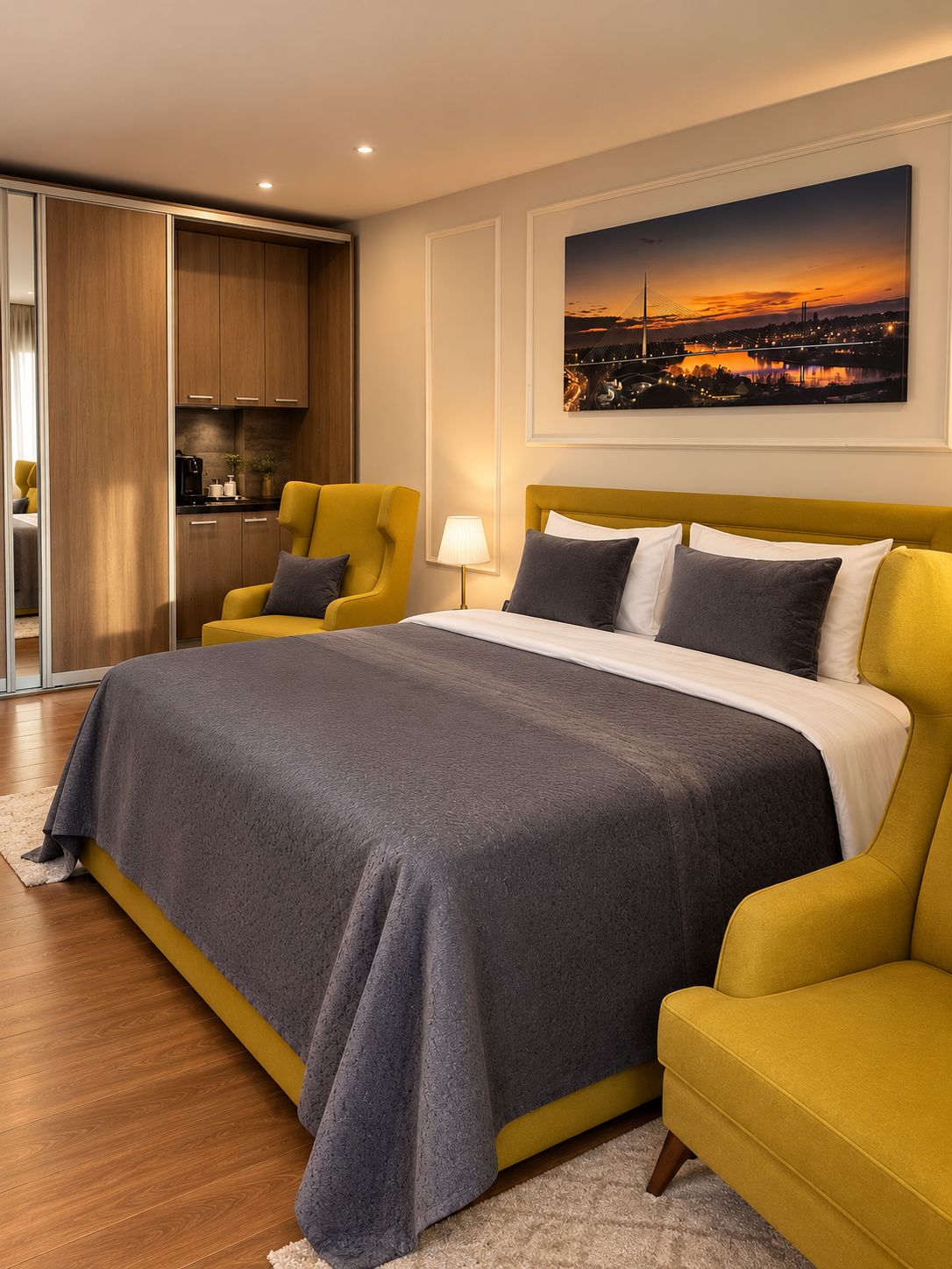 A modern hotel room with a large bed, a yellow armchair, a dining area, and a cityscape painting on the wall.