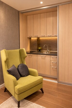 A modern kitchen with wooden cabinets, a stainless steel sink, and a green armchair with cushions.
