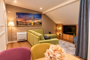 A modern living room with a sectional sofa, a flat-screen TV, a painting of a cityscape, and a small plant on a shelf. - Hotel Maksimum (Belgrade)