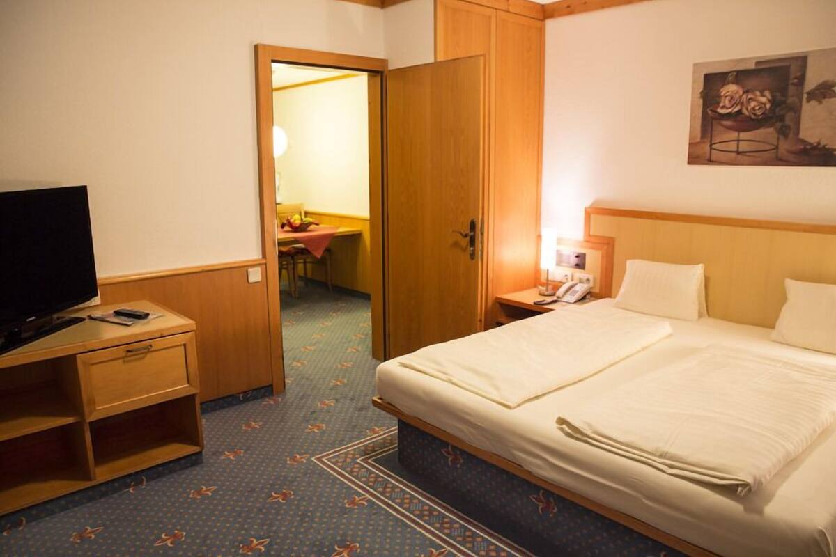 Une chambre d’hôtel comprenant un lit, un bureau avec une télévision, une armoire et une petite table avec une lampe.