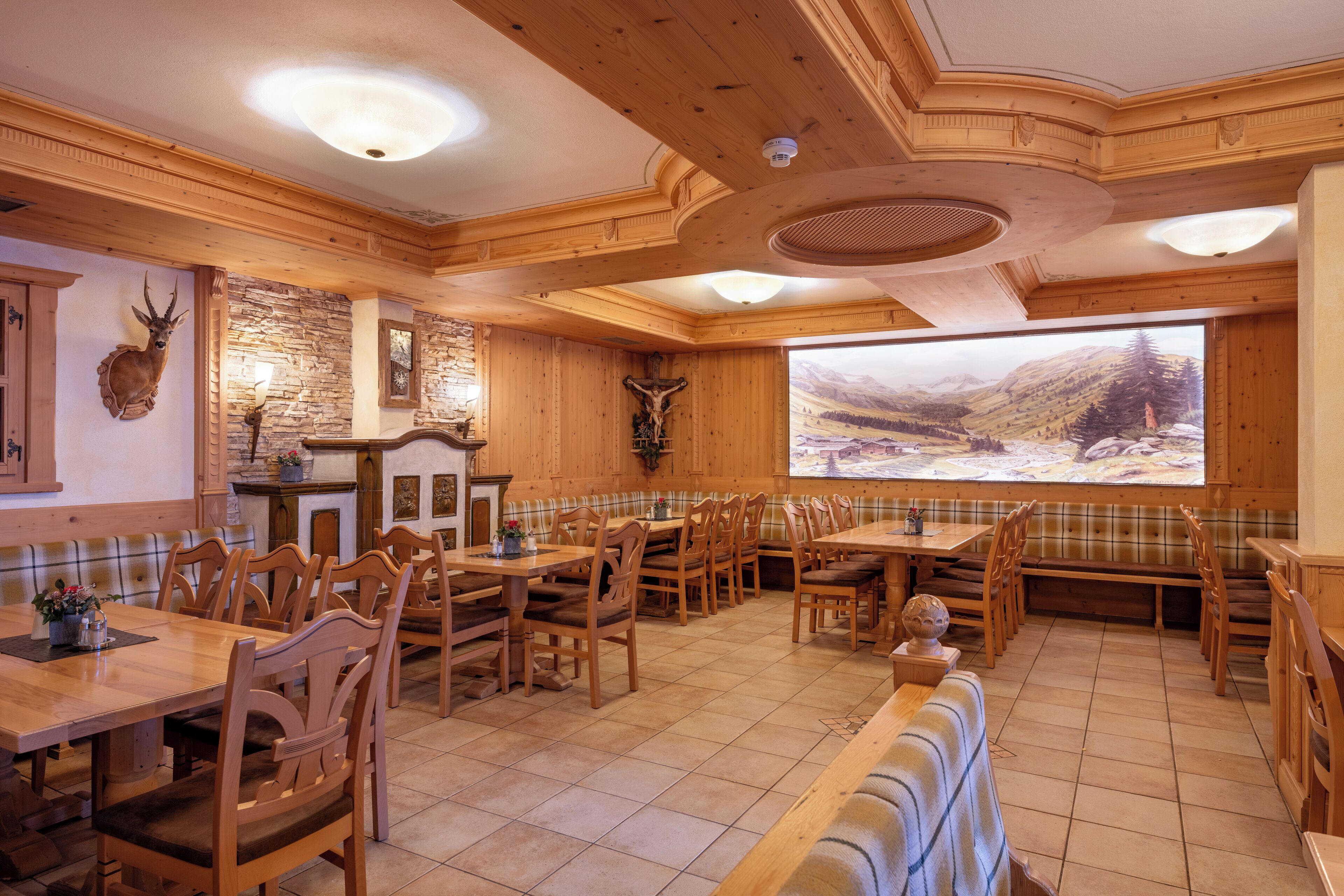 Ein Restaurant mit Holzeinrichtung, mehreren Tischen und Stühlen, einem großen Fenster mit schöner Aussicht und einem aufgehängten Hirschkopf an der Wand.